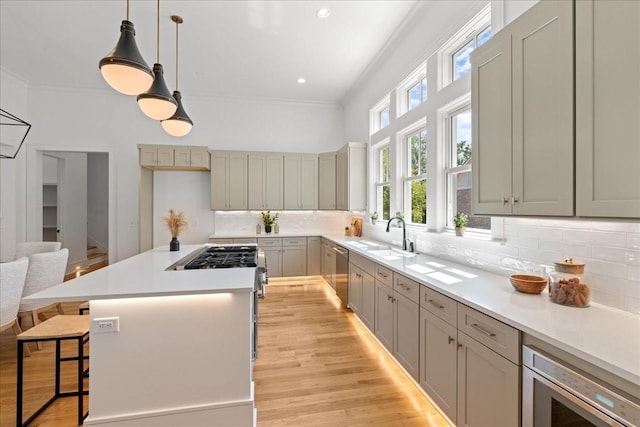 kitchen featuring gray cabinets, appliances with stainless steel finishes, a kitchen bar, sink, and decorative light fixtures