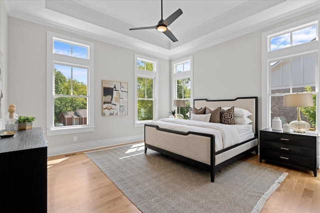 bedroom with ceiling fan, crown molding, light hardwood / wood-style floors, and a raised ceiling