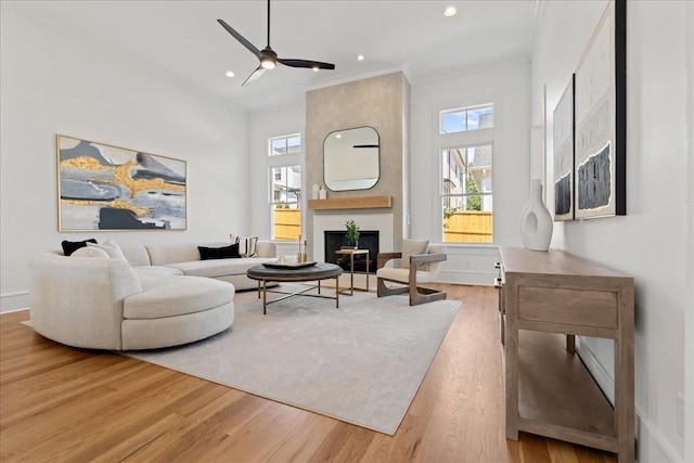 living room with a large fireplace, ceiling fan, ornamental molding, and hardwood / wood-style flooring