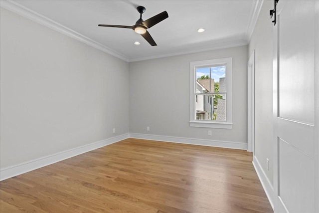 empty room featuring ceiling fan, ornamental molding, light wood-type flooring, and a barn door