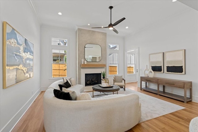 living room with a large fireplace, light wood-type flooring, ceiling fan, and ornamental molding