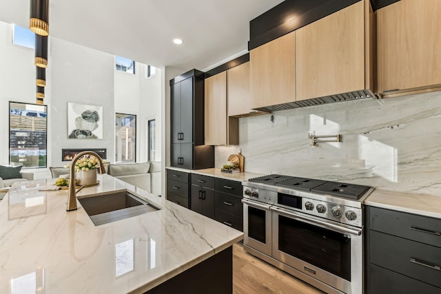 kitchen featuring range with two ovens, backsplash, light stone counters, and sink