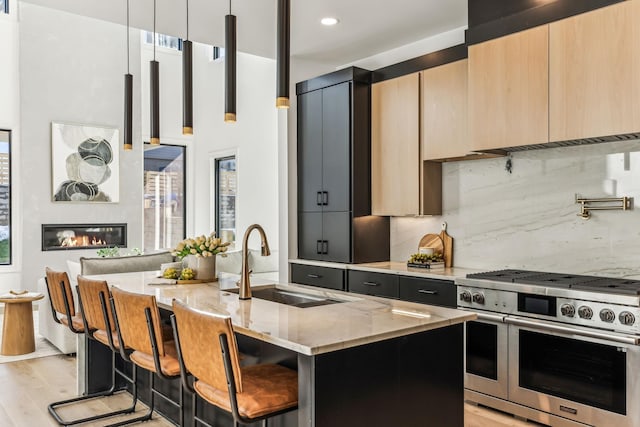 kitchen featuring a kitchen island with sink, light stone countertops, a breakfast bar, double oven range, and decorative light fixtures