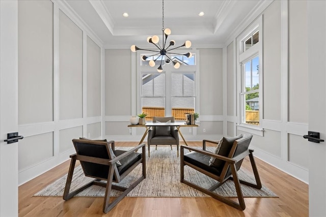 living area with crown molding, a raised ceiling, a notable chandelier, and light hardwood / wood-style flooring