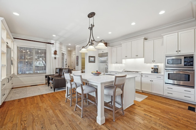 kitchen featuring built in appliances, white cabinetry, light hardwood / wood-style floors, and hanging light fixtures