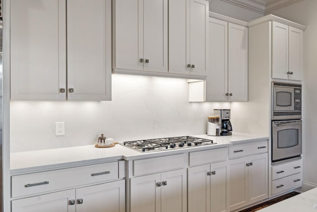 kitchen featuring stainless steel appliances, crown molding, light stone countertops, decorative backsplash, and white cabinetry