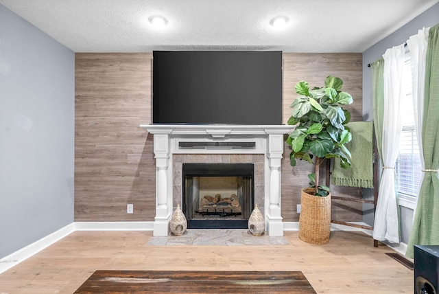 unfurnished living room featuring a tile fireplace, light wood-type flooring, wooden walls, and a textured ceiling