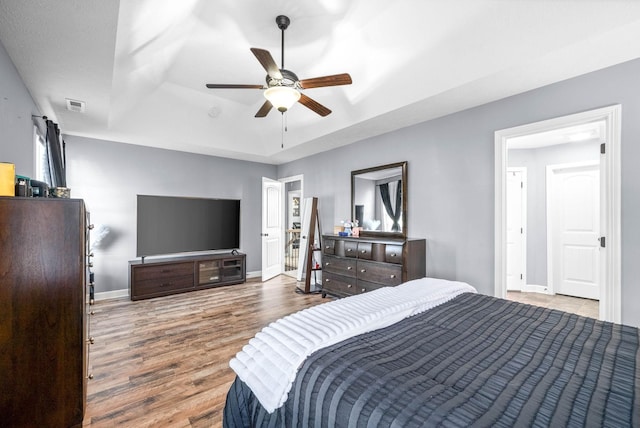 bedroom featuring hardwood / wood-style flooring, refrigerator, ceiling fan, and a tray ceiling