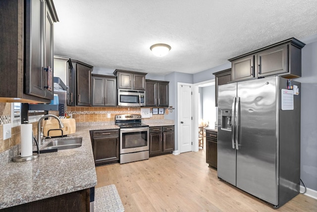 kitchen with light hardwood / wood-style flooring, stainless steel appliances, stone counters, dark brown cabinets, and sink