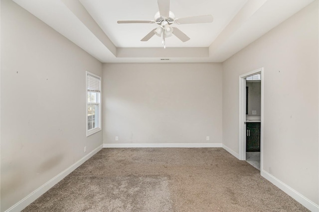 carpeted spare room with ceiling fan and a raised ceiling