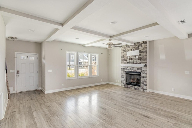 unfurnished living room with ceiling fan, beamed ceiling, a stone fireplace, and light hardwood / wood-style flooring