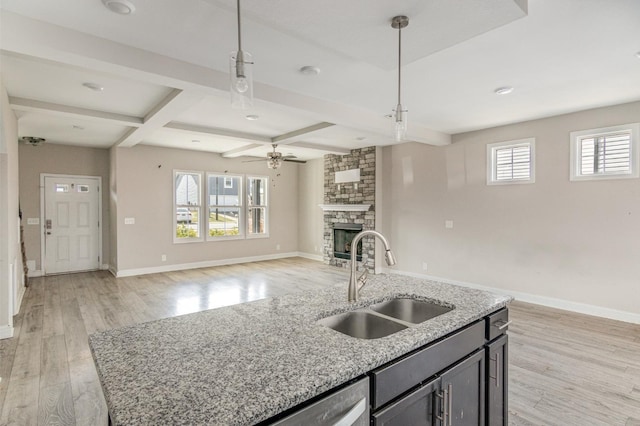 kitchen with a center island with sink, sink, a fireplace, hanging light fixtures, and beam ceiling