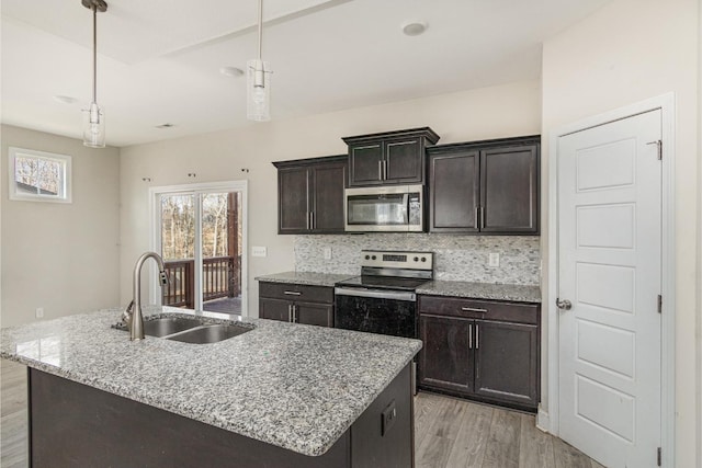 kitchen with an island with sink, hanging light fixtures, dark brown cabinetry, sink, and appliances with stainless steel finishes