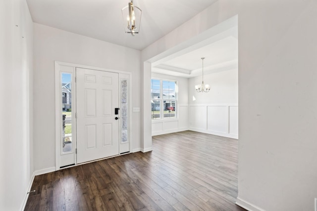 foyer with dark wood-type flooring, a chandelier, and a tray ceiling