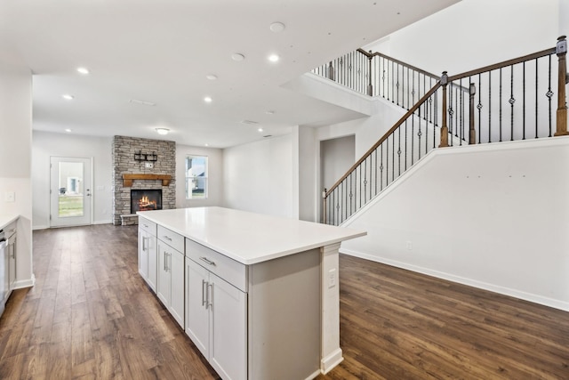 kitchen featuring white cabinets, a center island, dark wood-type flooring, and a stone fireplace