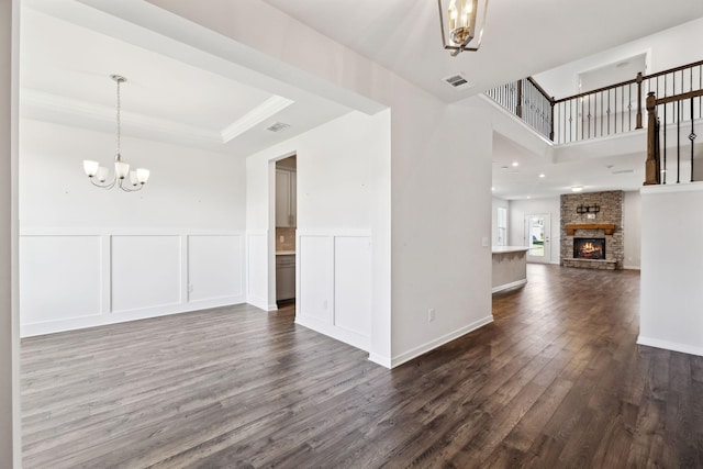 spare room with a stone fireplace, an inviting chandelier, and dark wood-type flooring