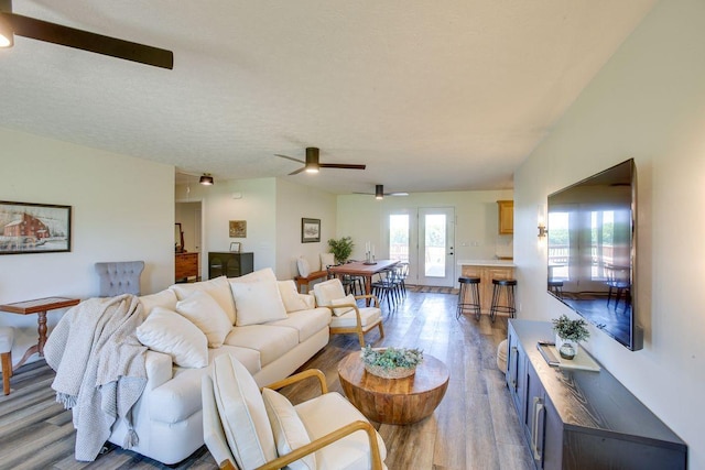 living room featuring ceiling fan, a textured ceiling, and light hardwood / wood-style floors