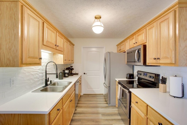 kitchen featuring appliances with stainless steel finishes, light brown cabinets, tasteful backsplash, light wood-type flooring, and sink