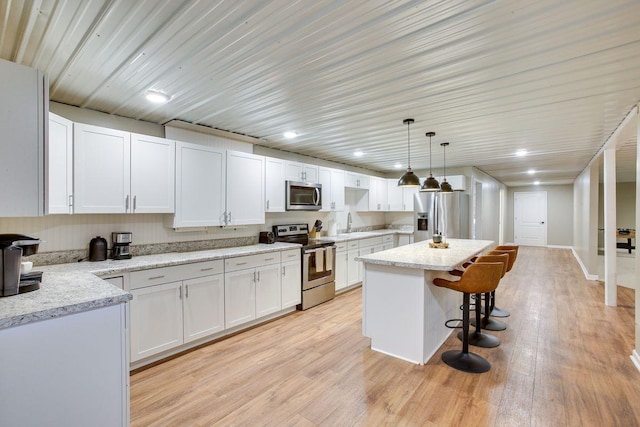 kitchen featuring hanging light fixtures, white cabinets, stainless steel appliances, and a kitchen island