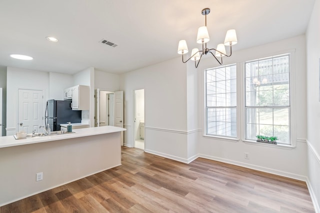 kitchen with black fridge, decorative light fixtures, a notable chandelier, light wood-type flooring, and white cabinets