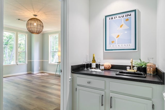 bar featuring hardwood / wood-style floors, ornamental molding, pendant lighting, sink, and white cabinetry