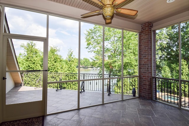 unfurnished sunroom featuring ceiling fan, wood ceiling, and a water view