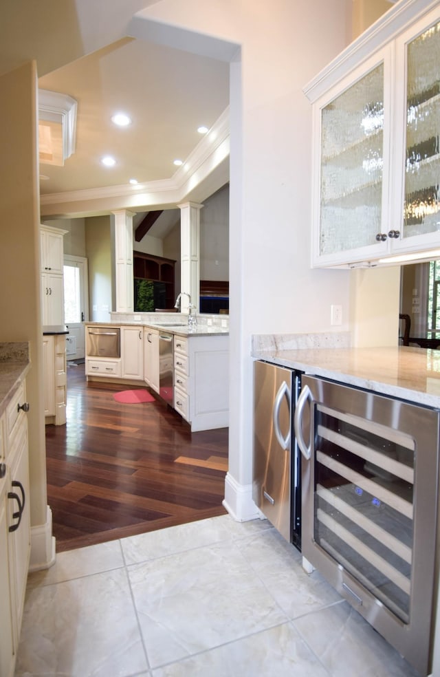 interior space featuring light stone counters, stainless steel dishwasher, beverage cooler, white cabinets, and ornamental molding