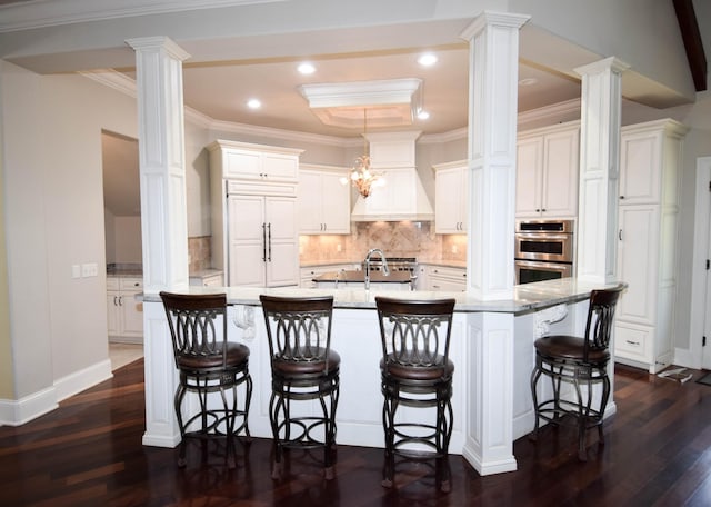 kitchen featuring double oven, a breakfast bar, white cabinetry, and a kitchen island with sink