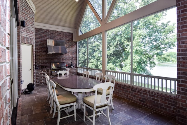 sunroom / solarium with a brick fireplace, vaulted ceiling, and a water view