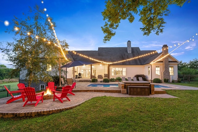 back house at dusk featuring an outdoor fire pit, a lawn, a swimming pool with hot tub, and a patio