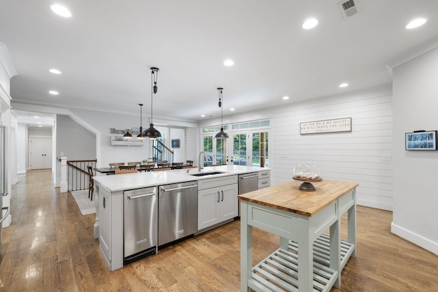 kitchen with sink, wooden walls, decorative light fixtures, an island with sink, and stainless steel dishwasher