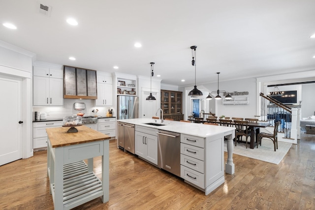 kitchen featuring decorative light fixtures, an island with sink, stainless steel appliances, white cabinets, and sink