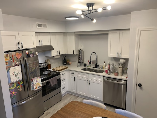 kitchen with light wood-type flooring, an inviting chandelier, white cabinetry, appliances with stainless steel finishes, and sink