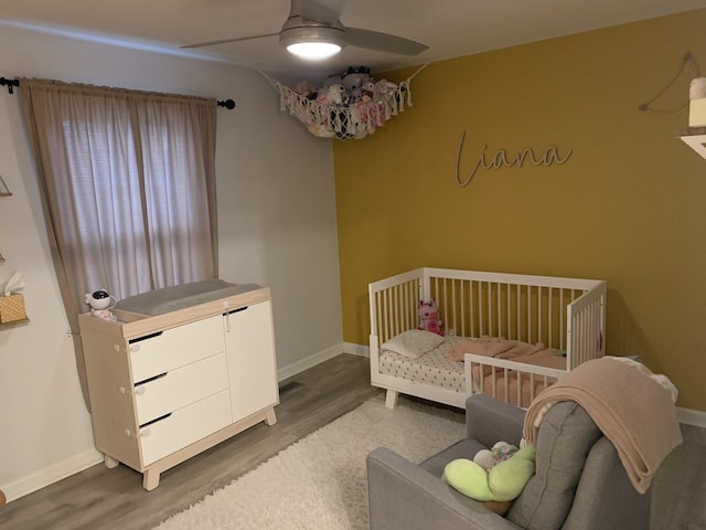 bedroom featuring a nursery area, ceiling fan, and dark hardwood / wood-style flooring