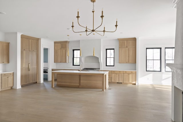 kitchen with light hardwood / wood-style floors, pendant lighting, light brown cabinetry, a kitchen island with sink, and a notable chandelier