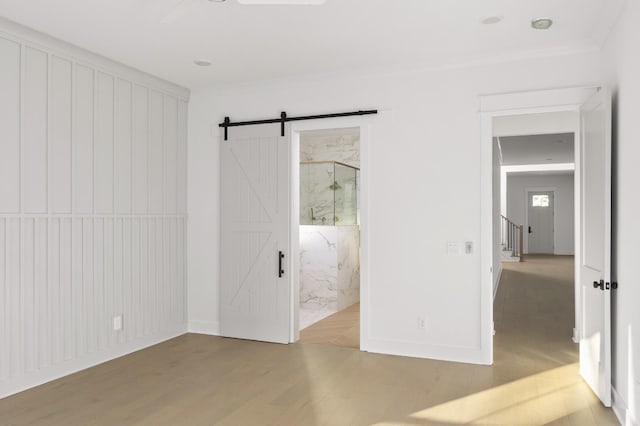 unfurnished bedroom featuring ensuite bathroom, a barn door, and wood-type flooring