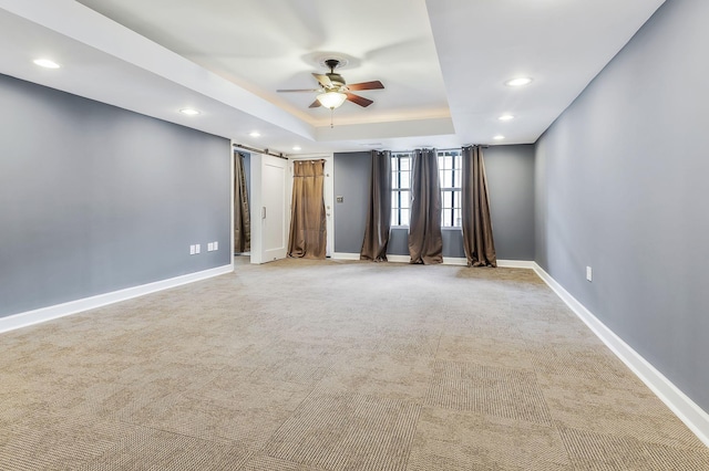 empty room featuring ceiling fan, light carpet, a barn door, and a tray ceiling