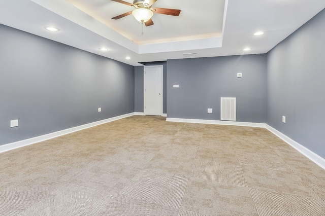 spare room with ceiling fan, a tray ceiling, and light carpet