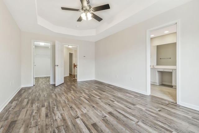 unfurnished bedroom with ensuite bath, a closet, a tray ceiling, a walk in closet, and ceiling fan