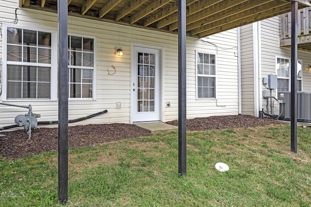 entrance to property featuring cooling unit and a lawn