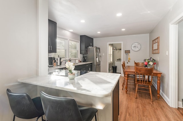 kitchen with kitchen peninsula, stainless steel fridge, a breakfast bar, light hardwood / wood-style floors, and black electric stovetop