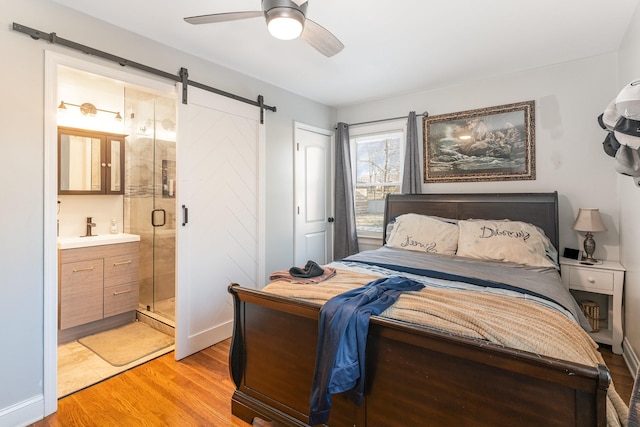 bedroom with sink, connected bathroom, ceiling fan, light hardwood / wood-style flooring, and a barn door