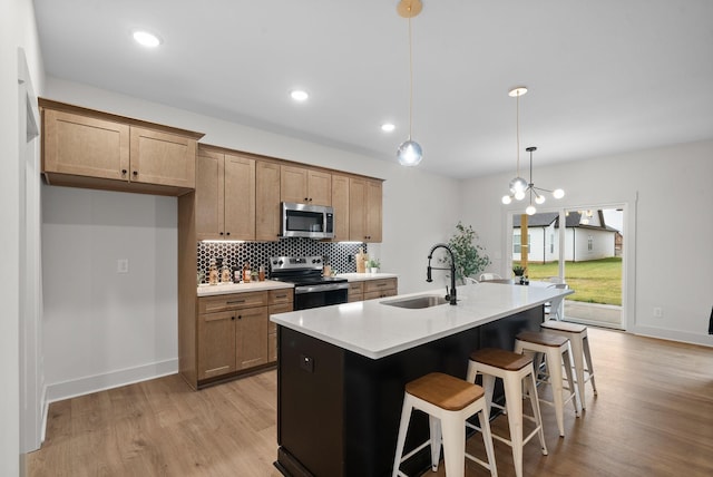 kitchen featuring sink, appliances with stainless steel finishes, a kitchen island with sink, hanging light fixtures, and tasteful backsplash