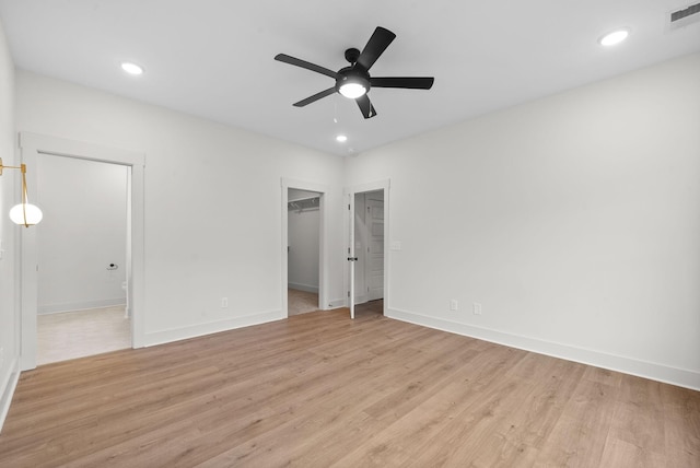 unfurnished bedroom featuring ceiling fan, a walk in closet, light hardwood / wood-style floors, and a closet