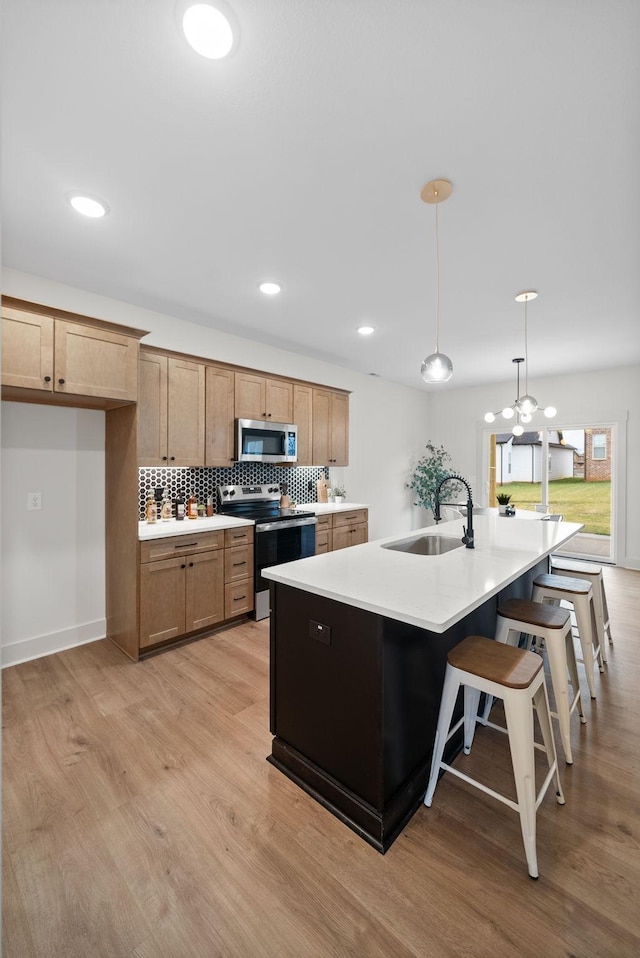 kitchen with pendant lighting, sink, stainless steel appliances, light hardwood / wood-style floors, and an island with sink