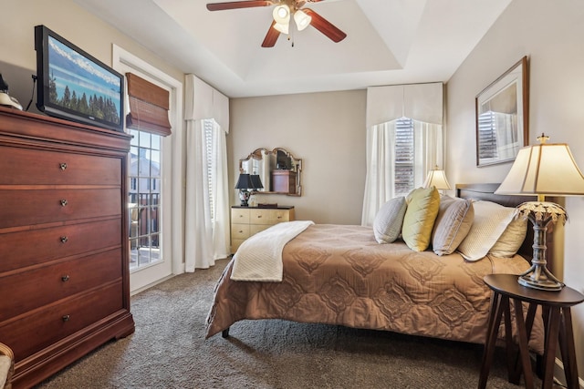 bedroom with a raised ceiling, ceiling fan, and dark colored carpet