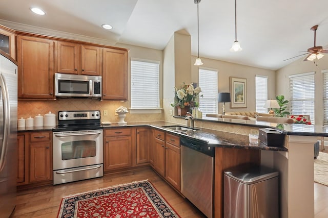 kitchen featuring appliances with stainless steel finishes, kitchen peninsula, pendant lighting, sink, and lofted ceiling