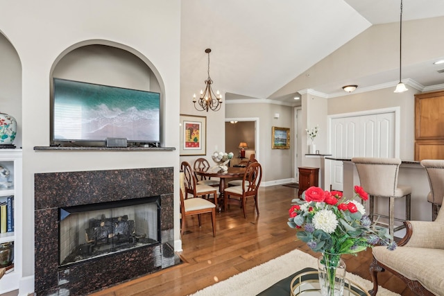 living room with vaulted ceiling, a chandelier, a premium fireplace, crown molding, and wood-type flooring