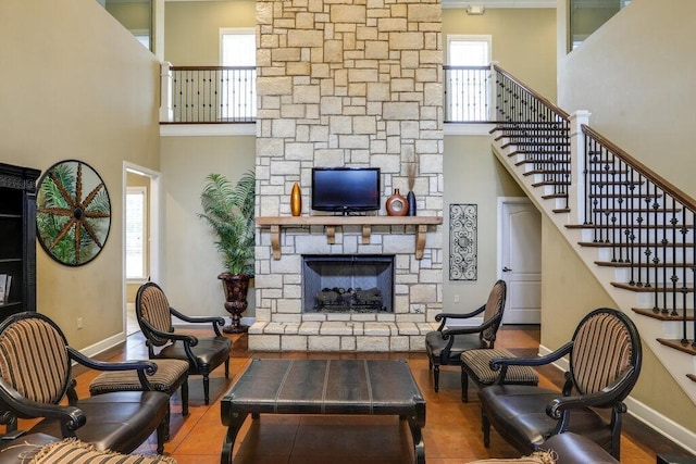 living room featuring a stone fireplace, a towering ceiling, and plenty of natural light