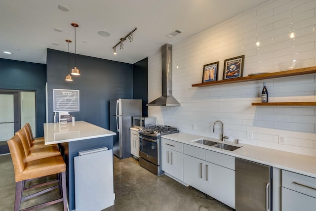 kitchen featuring appliances with stainless steel finishes, hanging light fixtures, wall chimney exhaust hood, white cabinets, and sink